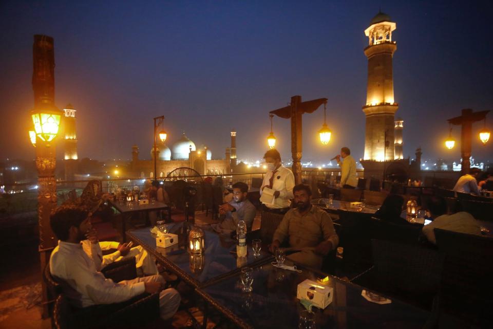 People eat at a rooftop restaurant close to the historical Badshahi Mosque, following an ease in restrictions that had been imposed to help control the coronavirus, in Lahore, Pakistan, Tuesday, Aug. 11, 2020. Pakistan's daily virus infection rate has stayed under 1,000 for more than four weeks prompting the government to further ease restrictions for restaurants, parks, gyms and cinemas. (AP Photo/K.M. Chaudary)