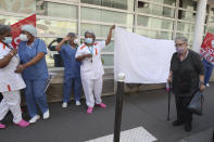 An elderly woman walks past employees demonstrating outside a nursing home of the Korian group, one of the market leaders in the lucrative industry of providing care and assisted living facilities for older adults, Monday, May 25, 2020 in Paris. In France, the group is facing several lawsuits filed by families who have lost loved ones during the coronavirus pandemic that has caused thousands of deaths in French care homes. (AP Photo/Thibault Camus)