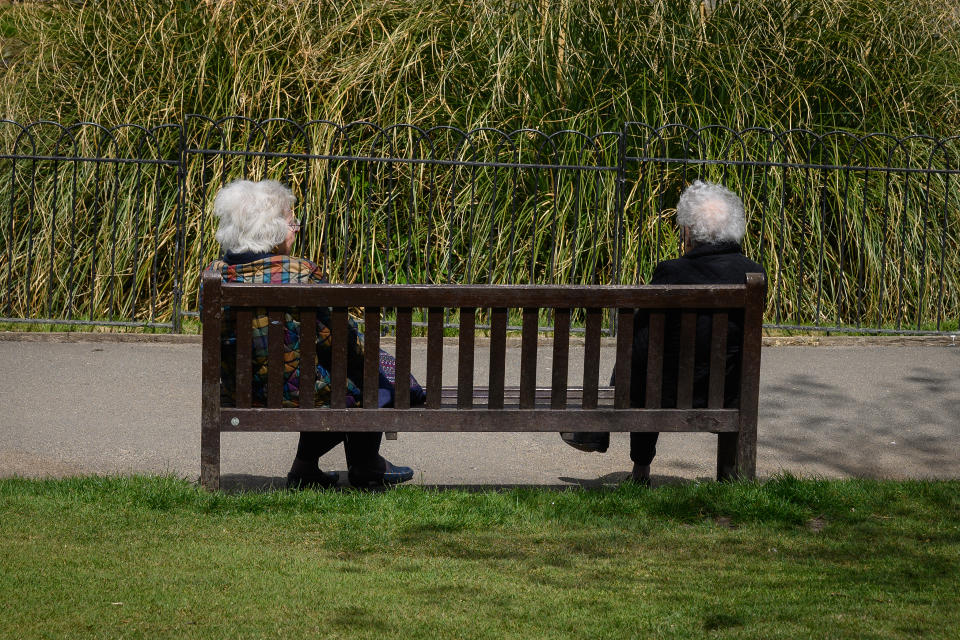 Two elderly women keep their distance as they chat on a bench in Golders Hill Park, London.