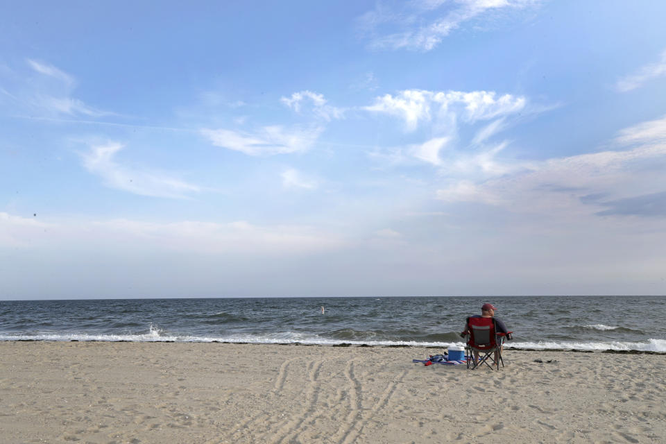 In this Aug. 21, 2019 photo, a man enjoys the view at Covell Beach in Centerville, Mass. Vineyard Winds' proposed buried energy cables would stretch from offshore wind turbines, through the ocean, under the sand and parking lot at Covell Beach, to a landing point where the cables would then extend to a grid connection inland. But as Trump has made clear how much he hates wind turbines, all the offshore wind projects, including the nation's first utility-scale offshore wind project, an 84 turbine, $2.8 billion wind farm slated to rise 15 miles off Martha's Vineyard, have stalled. (AP Photo/Elise Amendola)