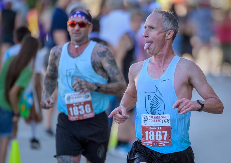 Steamboat Hall of Fame inductee Dan Gray sticks out his tongue playfully at well-wishers near the finish line of the 2022 Steamboat Classic 15K race Saturday, June 18, 2022 in downtown Peoria. Close on his heels is RC Outfitters owner and longtime Peoria running advocate Adam White.