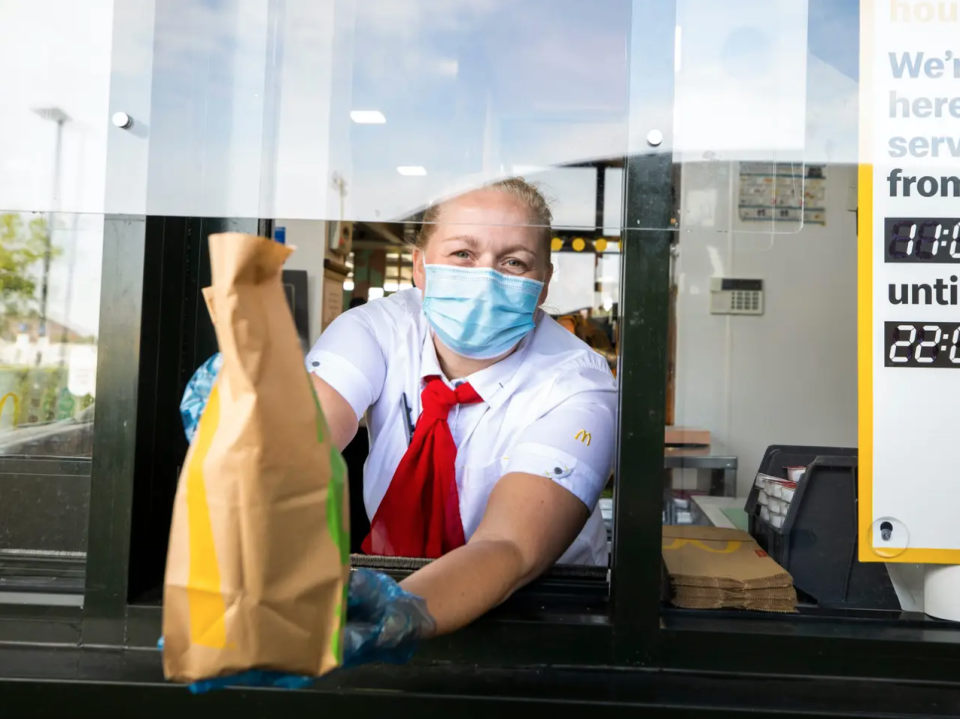 Eine McDonald's-Mitarbeiterin, die einem Kunden die Tüte mit dem Essen überreicht. - Copyright: Liam McBurney/PA Images via Getty Images