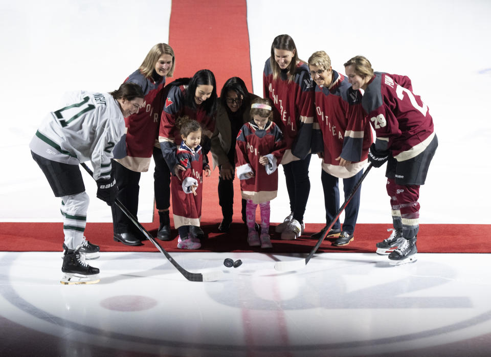 Boston's Hilary Knight (21) and Montreal's Marie-Philip Poulin (29) pose for a ceremonial puck drop with, from left to right, France St-Louis, Caroline Ouellette, her children Tessa and Liv, Danielle Sauvageau, Kim St-Pierre, and Danielle Goyette, prior to a PWHL hockey game in Montreal, Saturday, Jan. 13, 2024. (Christinne Muschi/The Canadian Press via AP)