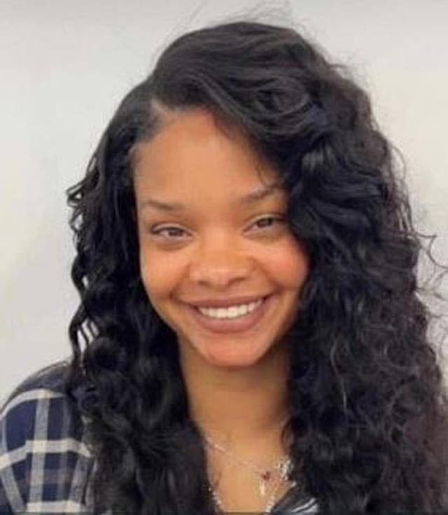 Photo of a young woman in a blue checked shirt with long, dark and curly hair. She is smiling