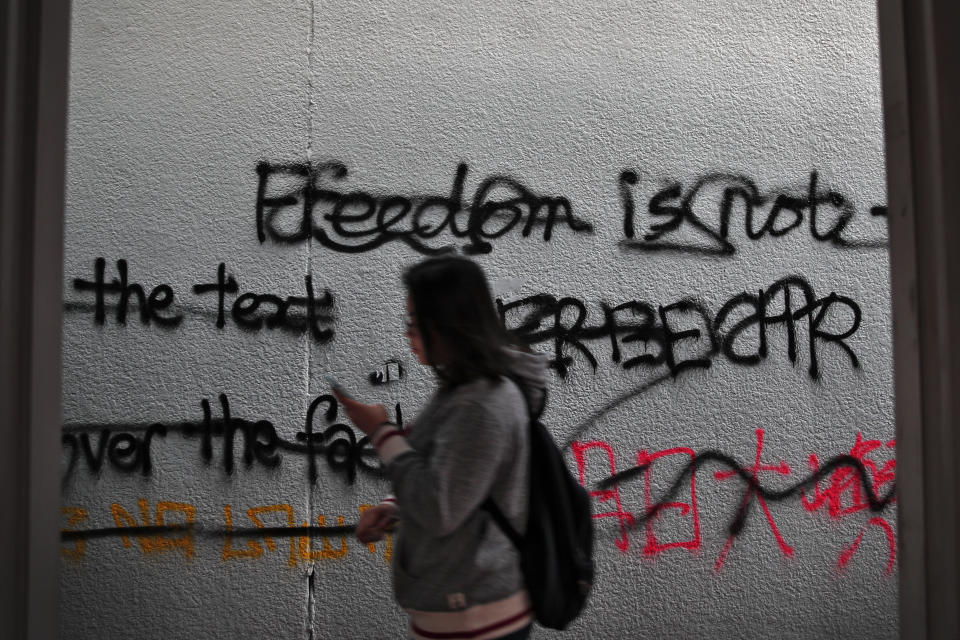 A woman walks by a wall sprayed by protest wording by pro-democracy protesters in Hong Kong, Saturday, Jan. 4, 2020. The months-long pro-democracy movement has extended into 2020 with further mass demonstrations. (AP Photo/Andy Wong)