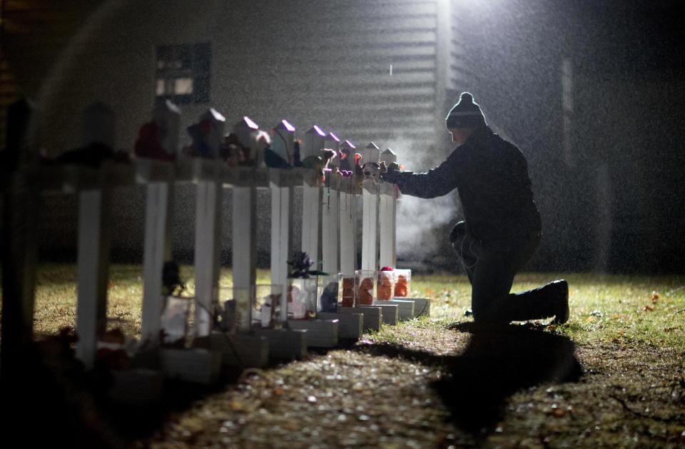 FILE - Frank Kulick, adjusts a display of wooden crosses, and a Jewish Star of David, representing the victims of the Sandy Hook Elementary School shooting, on his front lawn, Monday, Dec. 17, 2012, in Newtown, Conn. After a weekend of gun violence in America, Saturday, May 14, 2022, when shootings killed and wounded people grocery shopping, going to church and simply living their lives, the nation marked a milestone of 1 million deaths from COVID-19. The number, once unthinkable, is now a pedestrian reality in the United States, just as is the reality of the continuing epidemic of gun violence that kills tens of thousands of people a year. (AP Photo/David Goldman, File)