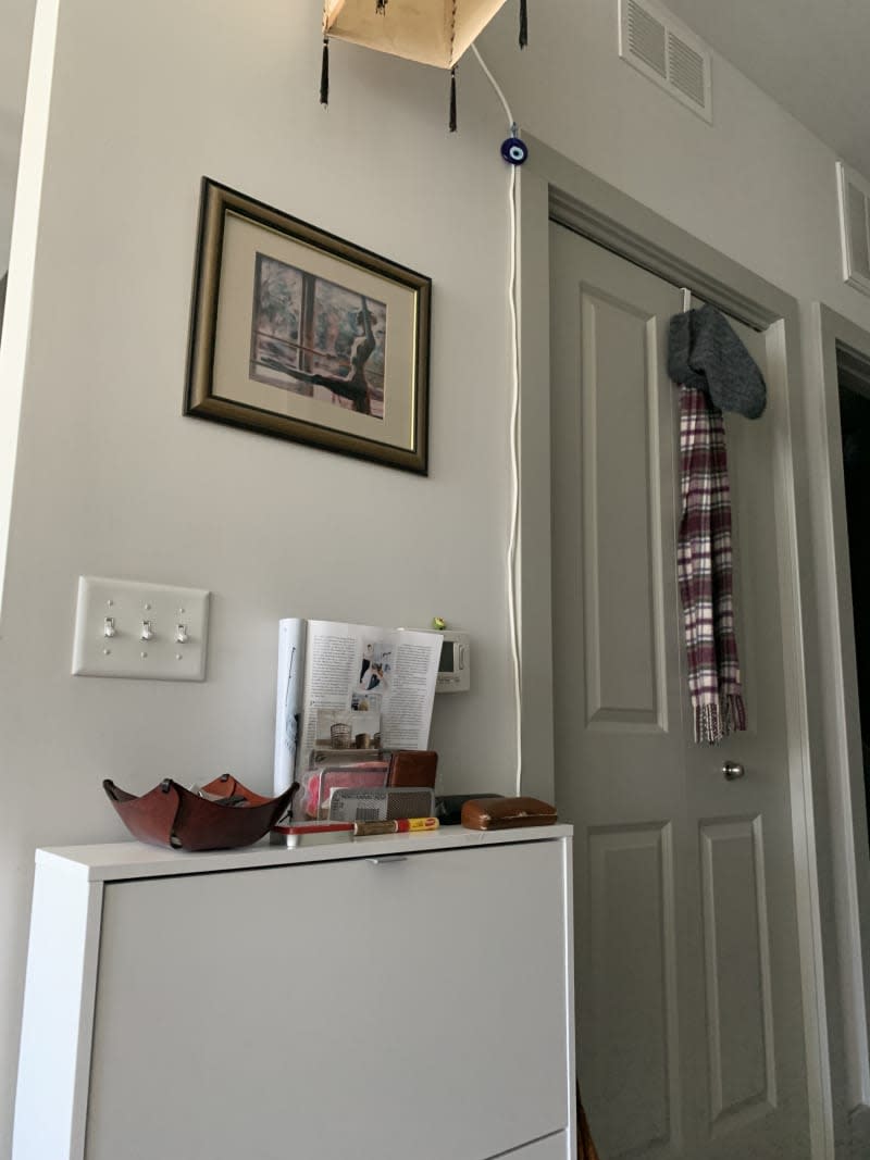 Framed photos over an entryway with various items stored atop a shelf.