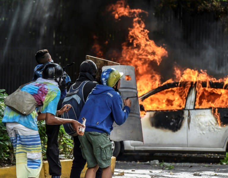 Anti-government demonstrators take cover behind shields near a burning car during clashes near Altamira Square in Caracas, on June 14, 2017