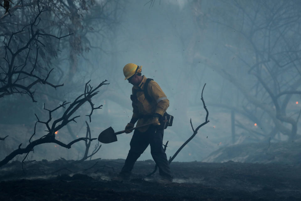 A firefighter works to put out hot spots on a fast moving wind-driven wildfire in Orange, California.