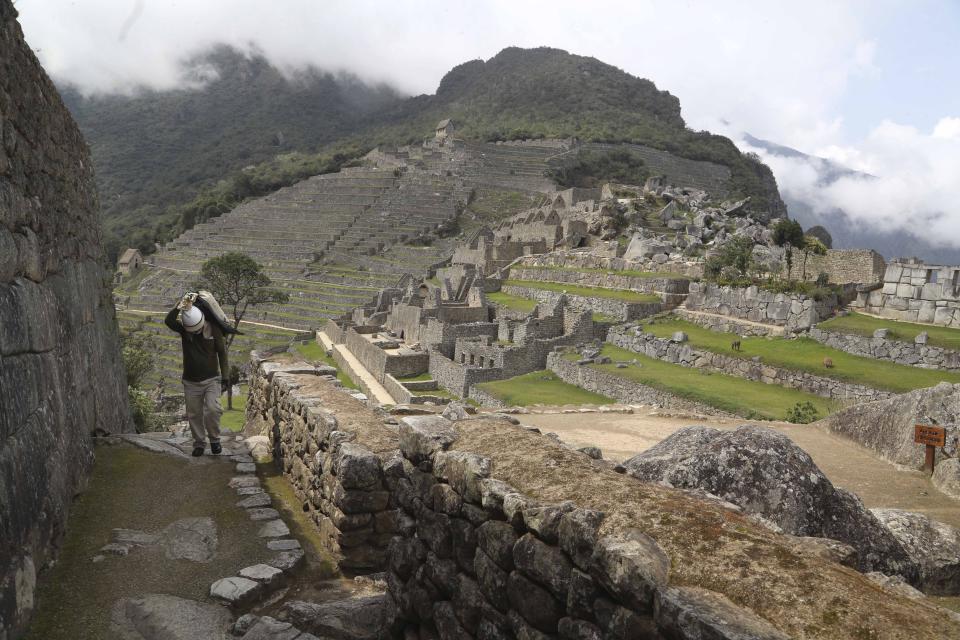 A maintenance worker carries a bag of stones at the Machu Picchu archeological site that's closed to the public amid the COVID-19 pandemic in the department of Cusco, Peru, Tuesday, Oct. 27, 2020. The world-renown Incan citadel of Machu Picchu will reopen to the public on Nov. 1. (AP Photo/Martin Mejia)