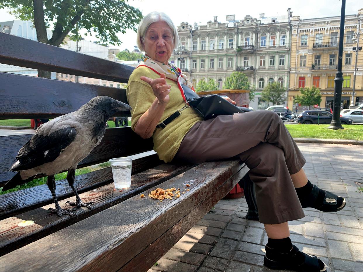 This picture taken with a smartphone shows an elderly woman gesturing to a crow as they sit on a bench during a warm spring day, in the centre of the Ukrainian capital Kyiv (AFP via Getty Images)