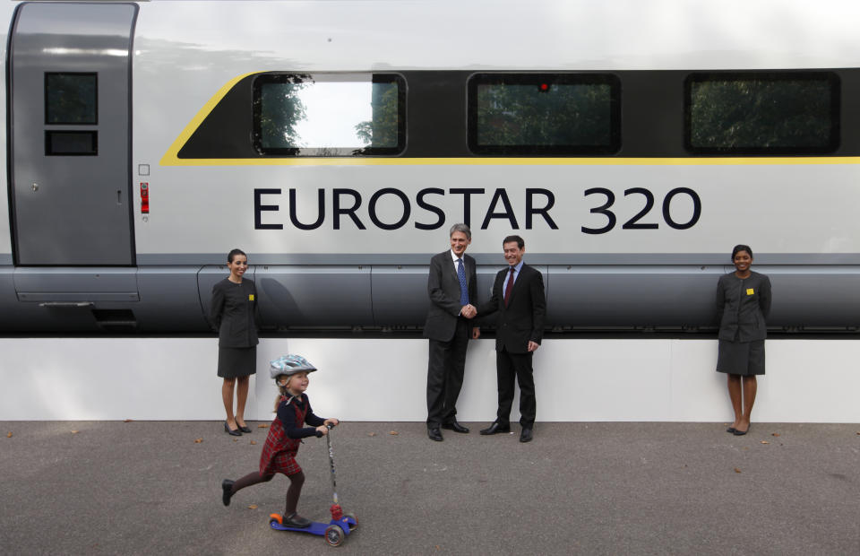 A child rides her scooter past Britain's Transport Minister Philip Hammond (2nd L) and Eurostar's Chief Executive Officer Nicolas Petrovic, as they shake hands next to a new Eurostar train, during a media event, in central London, October 7, 2010. German industrial group Siemens will supply 10 next-generation high-speed trains to Eurostar as part of a 700 million pound ($1 billion) investment in the Channel Tunnel operator's fleet. REUTERS/Andrew Winning (BRITAIN - Tags: BUSINESS POLITICS SOCIETY TRANSPORT TRAVEL)