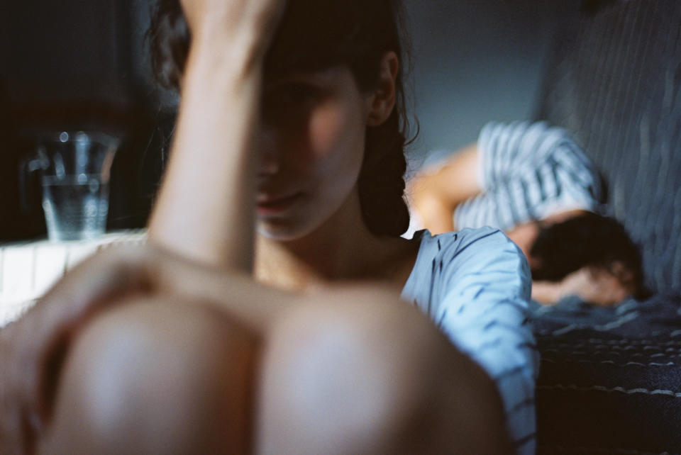 A woman is sitting at the edge of a bed, visibly upset