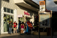 People walk by shops at the Whalers Village shopping mall, Wednesday, Dec. 6, 2023, in Lahaina, Hawaii. Residents and survivors still dealing with the aftermath of the August wildfires in Lahaina have mixed feelings as tourists begin to return to the west side of Maui. (AP Photo/Lindsey Wasson)