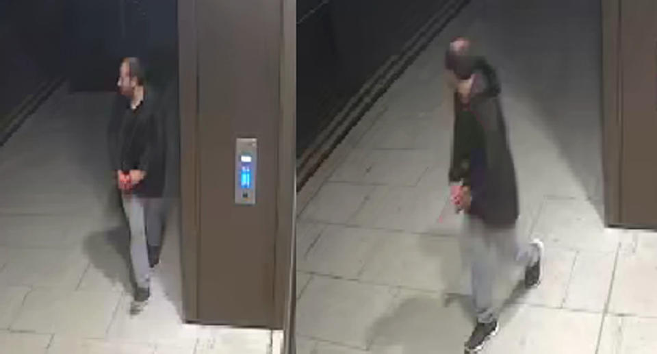 CCTV footage of man looking over his shoulder near a lift wearing light coloured jeans and a black hoodie.