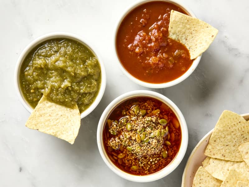 overhead shot of three different salsas: tomatillo, chipotle and salsa macha, in small bowls, with chips being dipped