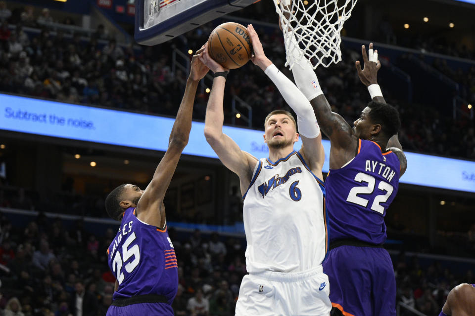 Washington Wizards center Kristaps Porzingis (6) goes to the basket against Phoenix Suns forward Mikal Bridges (25) and center Deandre Ayton (22) during the second half of an NBA basketball game Wednesday, Dec. 28, 2022, in Washington. The Wizards won 127-102. (AP Photo/Nick Wass)
