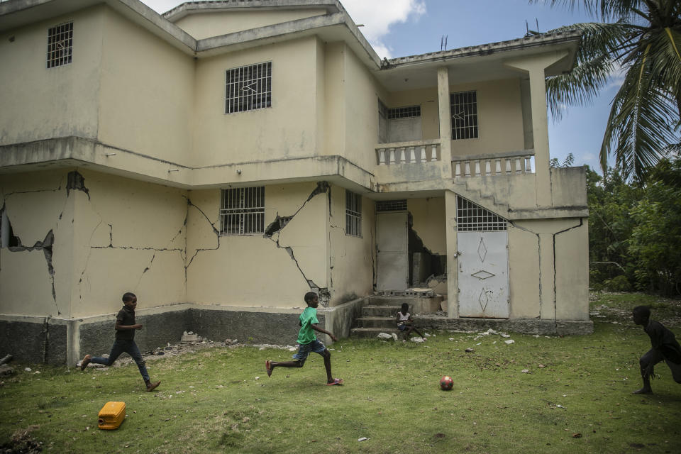 Children play football next to a house damaged a year ago by a magnitude-7.2 earthquake, in Maniche, Haiti, Thursday, Aug. 18, 2022. The home was among the more than 130,000 damaged or destroyed by the quake that struck southern Haiti last year, killing more than 2,200 people. (AP Photo/Odelyn Joseph)