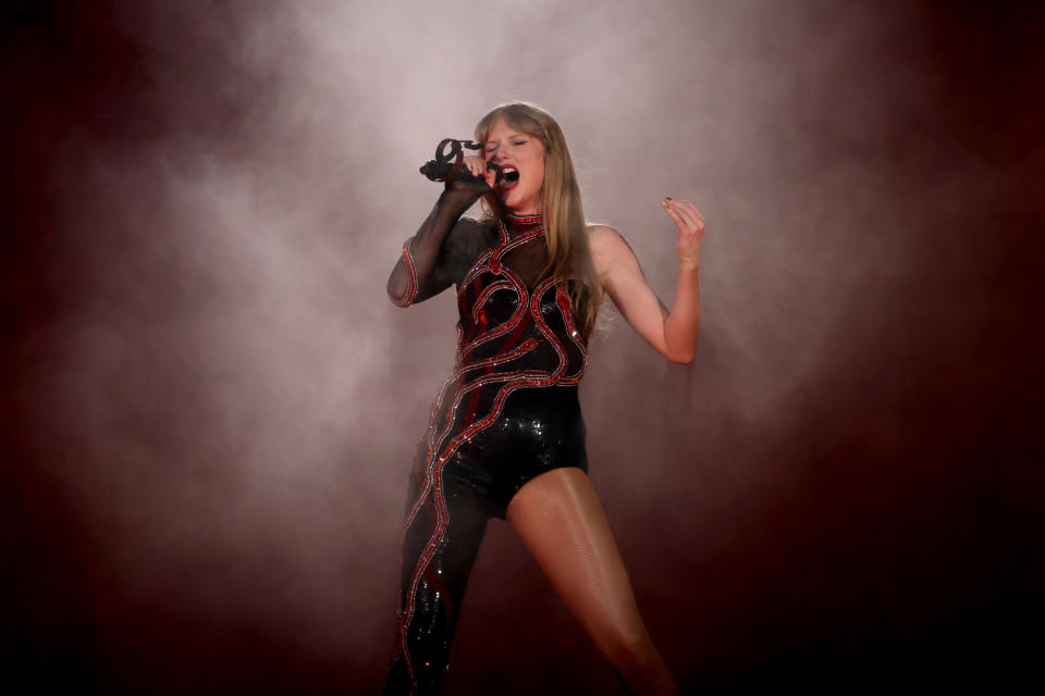 Taylor Swift singing on stage in a sparkly outfit with a smoky backdrop