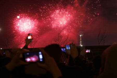 Visitors take pictures and videos as fireworks explode over Oriental Pearl Tower as part of a New Year countdown celebration on the Bund in Shanghai