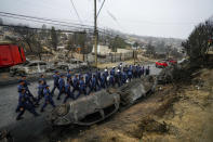 Chilean Navy personnel walk past overturned, charred cars as they deploy to help aid the Villa Independencia neighborhood after a forest fire reached Vina del Mar, Chile, Tuesday, Feb. 6, 2024. (AP Photo/Esteban Felix)