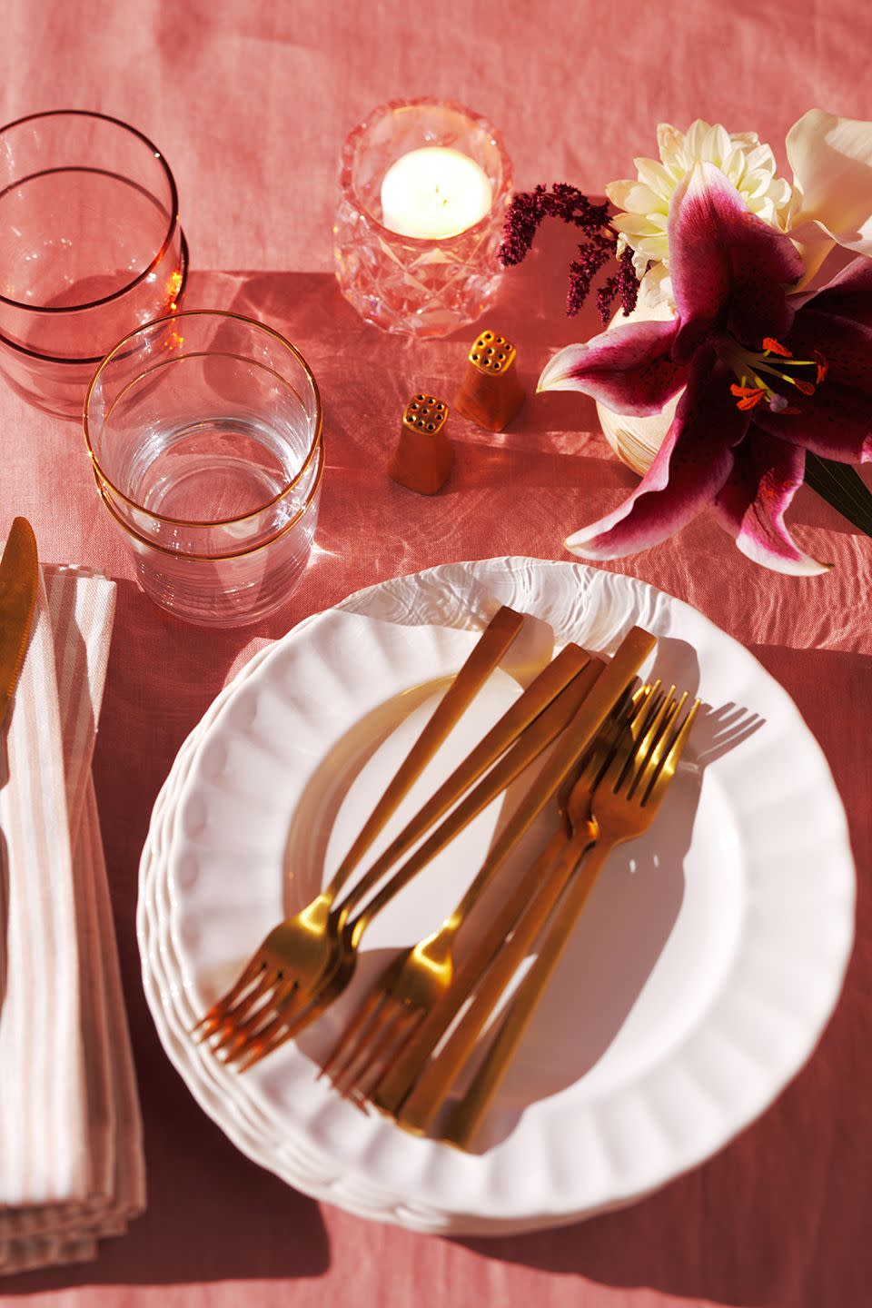 overhead shot of white scalloped plates with gold utensils on top of a pink table cloth