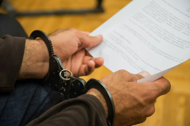 A migrant man wearing handcuffs holds an official paper as he sits in the dock of the county court in Szeged, Hungary on September 16, 2015