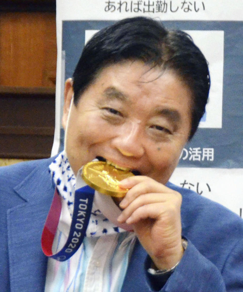 Nagoya Mayor Takashi Kawamura bites the Olympic gold medal of Miu Goto, a member of Japan softball team who won the event at the 2020 Summer Olympics, at the city office building in Nagoya, central Japan, Wednesday, Aug. 4, 2021. (Kyodo News via AP)