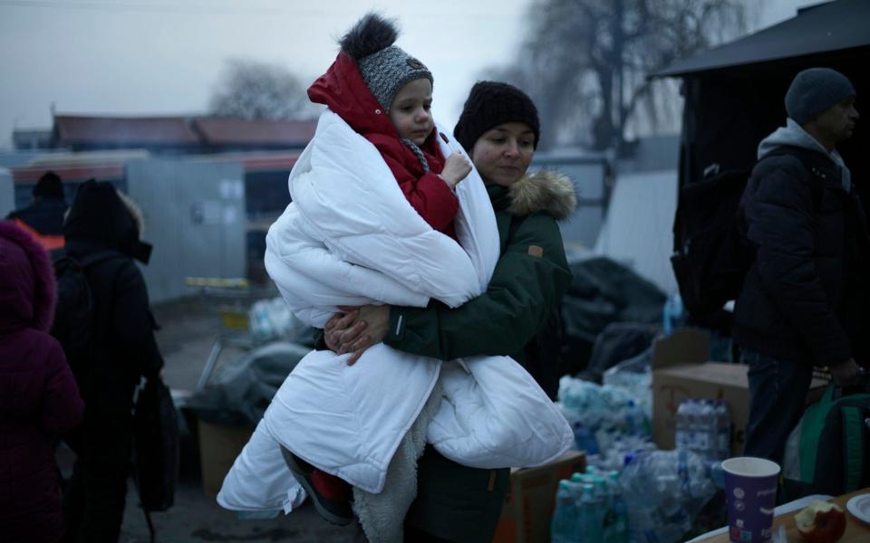 A woman carries a child wrapped in a blanket as she waits at a refugee crossing in Medyka, Poland - Markus Schreiber /AP