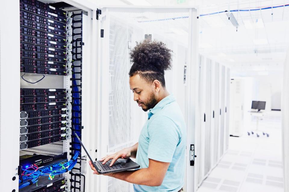 An IT professional analyzing a laptop connected to a server.