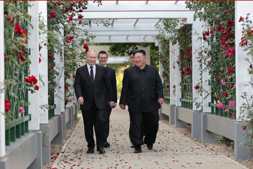 Kim Jong Un and Vladimir Putin walk with translators in a garden.