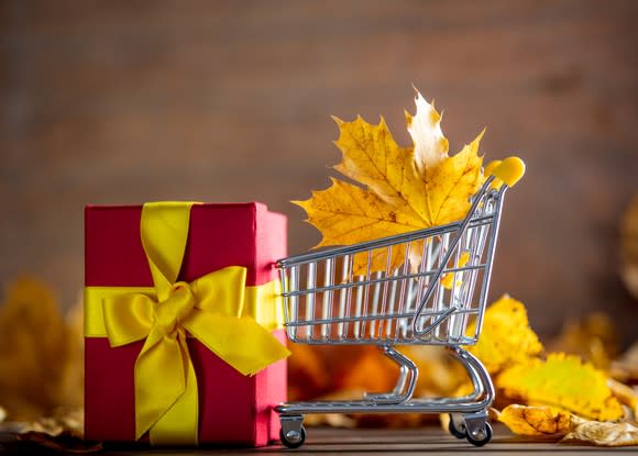 A maple leaf is in a tiny shopping cart near a small present.