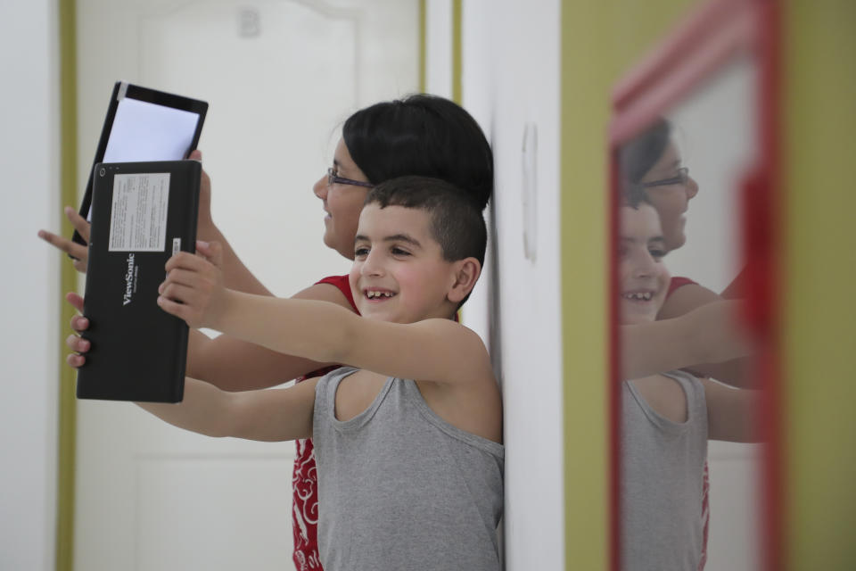 En esta imagen del 13 de marzo de 2017, los niños sirios Hosip, al frente, y Judy, al fondo, se hacen fotos con tabletas en su nueva casa de La Punta, en San Luis, Argentina. El gobernador de la provincia argentina de San Luis ha recibido con alegría a inmigrantes sirios, en lo que se cree es el programa de inmigración más generoso de su clase en Sudamérica. (AP Foto/Nicolás Aguilera)