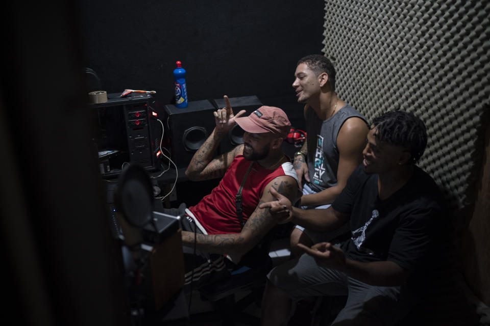 Trap de Cria artist Vitor Oliveira, known as "MC Piloto," right, reacts as Willian Santos "DJWillTrap" edits one of his tracks at his recording studio in the Rocinha slum of Rio de Janeiro, Brazil, Thursday, March 18, 2021. Oliveira has plowed all of his resources into transforming a tiny apartment into a recording studio and editing room, to which he returns to each night after driving his motorcycle taxi up and down one of Latin America’s largest slums. (AP Photo/Felipe Dana)