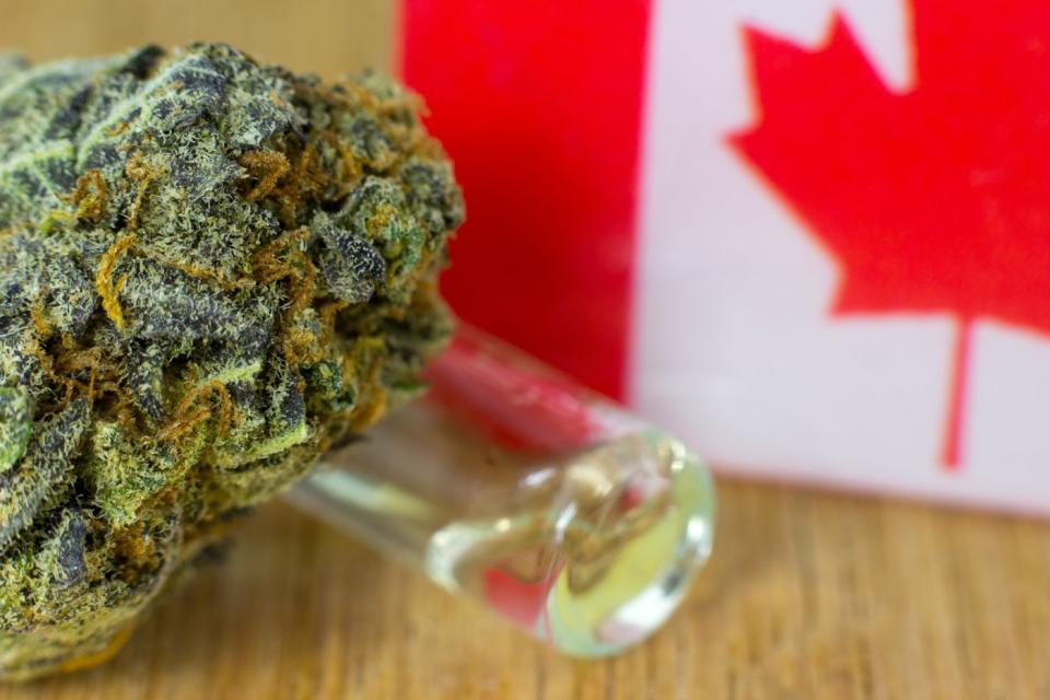 A dry cannabis bud and small vile of cannabidiol oil next to a miniature Canadian flag.