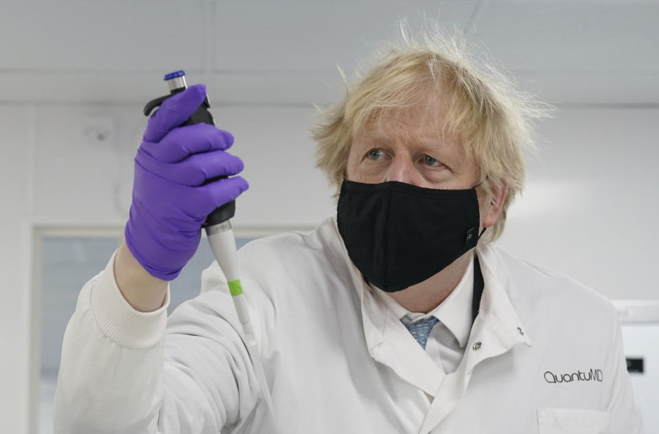 Britain's Prime Minister Boris Johnson looks at a pipette before him, during briefing by a molecular biologist at the QuantuMDx Biotechnology company in Newcastle, England on Saturday Feb.13, 2021. Johnson is visiting manufacturing facilities in north east England to see ongoing Covid-19 responses in the region. (Ian Forsyth/Pool via AP)