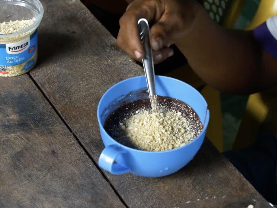 A hand holds a spoon in a bowl of açaí and dulce de leite.