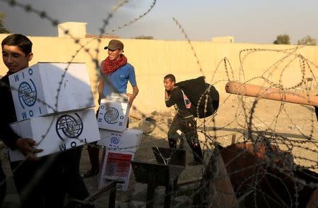 Newly displaced people carry humanitarian packages after they climbed over a wall to get them at a processing center in Qayyara, south of Mosul, Iraq October 25, 2016. REUTERS/Zohra Bensemra