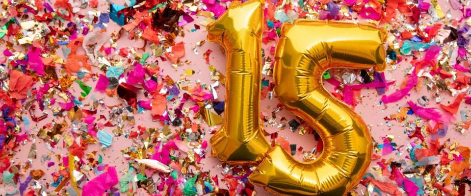 Number 15 gold birthday celebration balloon on a confetti glitter background