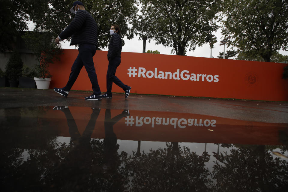 Una par de espectadores pasa por un charco de agua durante l primera jornada del Abierto de Francia, el domingo 27 de septiembre de 2020, en París. (AP Foto/Alessandra Tarantino)