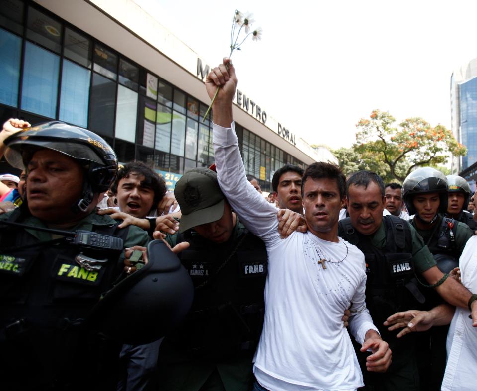 Opposition leader Leopoldo Lopez, dressed in white and holding up a flower stem, is taken into custody by Bolivarian National Guards, in Caracas, Venezuela, Tuesday, Feb 18, 2014. Lopez re-emerged from days of hiding to address an anti-government demonstration and then he turned himself in to authorities Tuesday. Speaking to some 5,000 supporters with a megaphone, Lopez said that he doesn't fear going to jail to defend his beliefs and constitutional right to peacefully protest against President Nicolas Maduro. (AP Photo/Alejandro Cegarra)