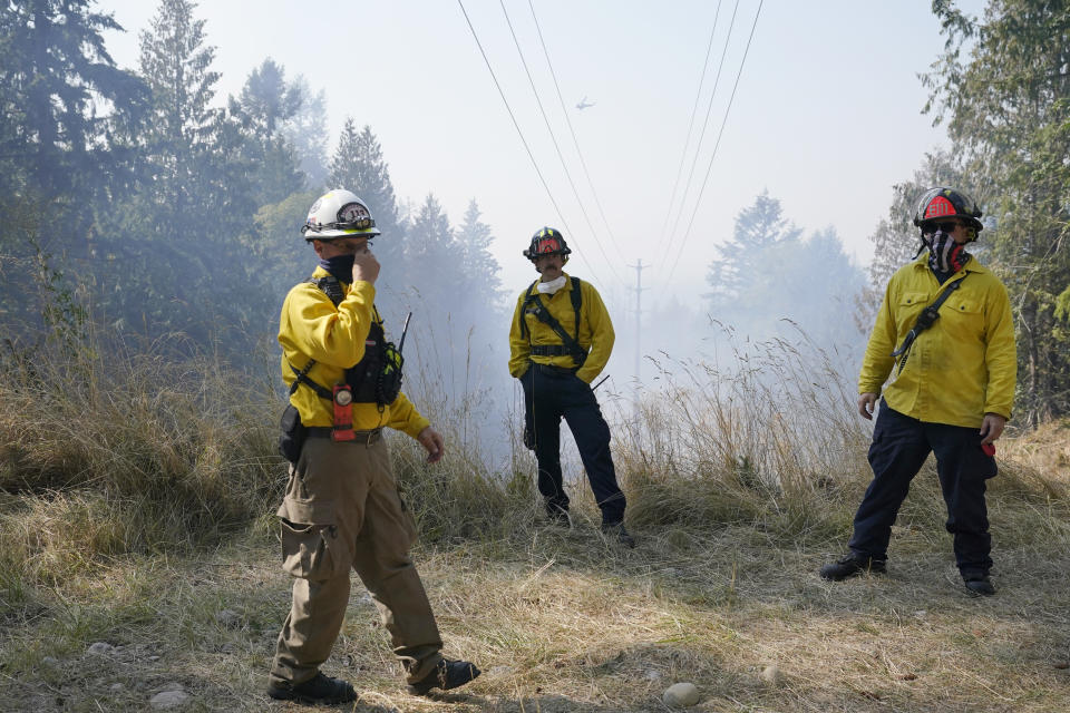 Firefighters wait under power lines for a helicopter to make a water drop, Wednesday, Sept. 9, 2020, on a hotspot of a wildfire burning in Bonney Lake, Wash., south of Seattle. (AP Photo/Ted S. Warren, Pool)