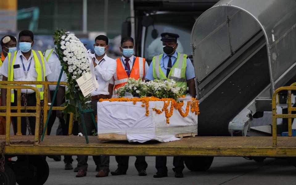 Sri Lankan air port workers stand next to a casket carrying remains of Priyantha Kumara, a Sri Lankan employee who was lynched by a Muslim mob in Sialkot last week after unloading it from an air craft in Colombo, Sri Lanka, Monday, Dec. 6, 2021. (AP Photo/Eranga Jayawardena)