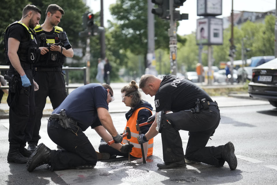 Policías alemanes utilizan martillos y cinceles para desalojar a un activista que se pegó a una carretera durante una protesta climática en Berlín, Alemania, el lunes 22 de mayo de 2023. (AP Foto/Markus Schreiber)