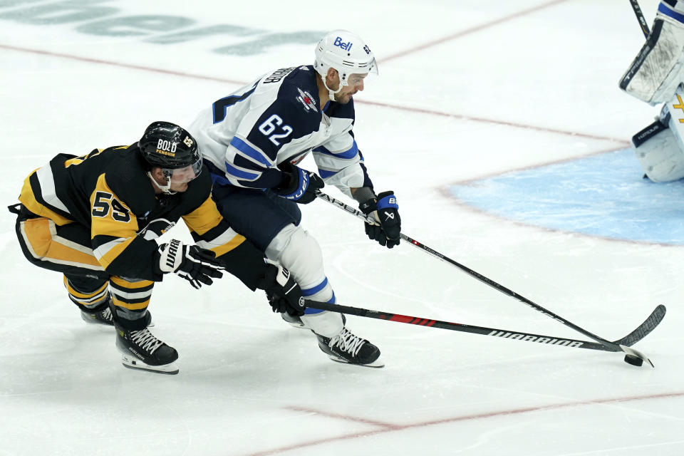 Pittsburgh Penguins' Noel Acciari (55) reaches for the puck behind Winnipeg Jets' Nino Niederreiter (62) during the first period of an NHL hockey game, Tuesday, Feb. 6, 2024, in Pittsburgh. (AP Photo/Matt Freed)