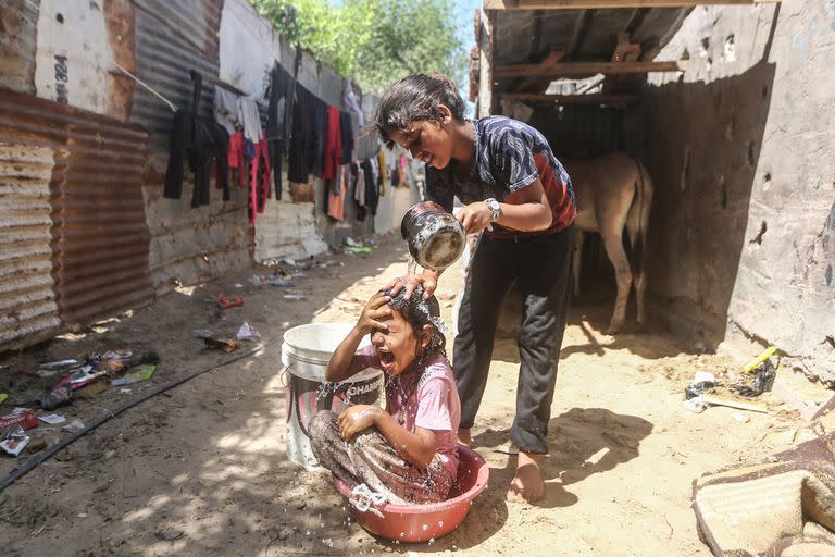 Una niña palestina vierte agua sobre otra, en medio de altas temperaturas y cortes de energía en Gaza, en julio de 2023