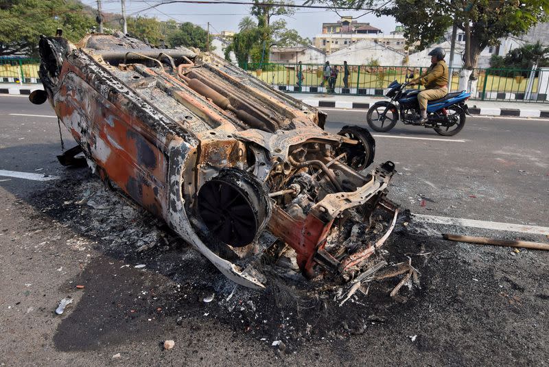 A policeman rides a motorcycle past a damaged vehicle that was set on fire by demonstrators during a protest after India's parliament passed a Citizenship Amendment Bill