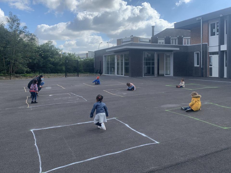 Pictured are a small number of children sitting inside a chalk-drawn square in a school playground. 