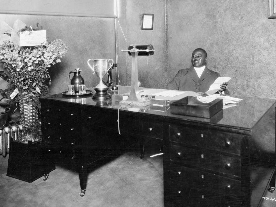 Black and white photo of Robert Sengstacke Abbott behind a large desk in an office.