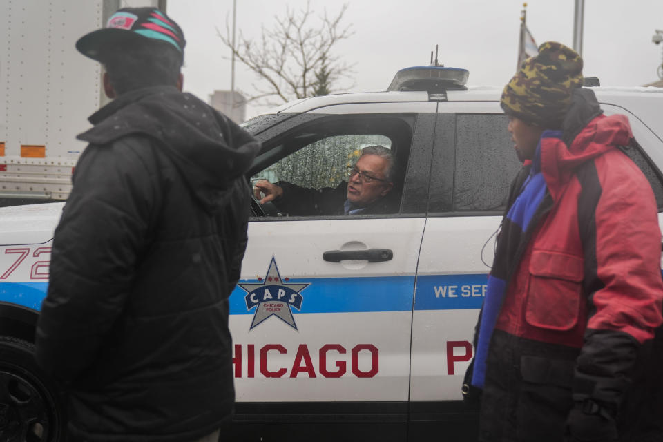 Citing safety concerns about migrants crossing the street in traffic, a Chicago police officer instructs Pastor Jonathan de la O of Starting Point Community Church to tell people to meet him down the street from where "warming" buses are parked in the 800 block of South Desplaines Street to receive food and clothing donations as a winter storm passes through Friday, Jan. 12, 2024, in Chicago. In the city of Chicago's latest attempt to provide shelter to incoming migrants, several buses were parked in the area to house people in cold winter weather. (AP Photo/Erin Hooley)
